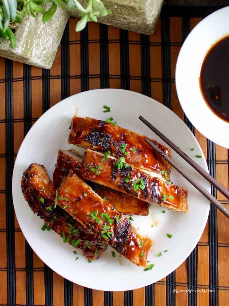 Overhead shot of Chinese style ribs stacked on a white plate with extra sauce.