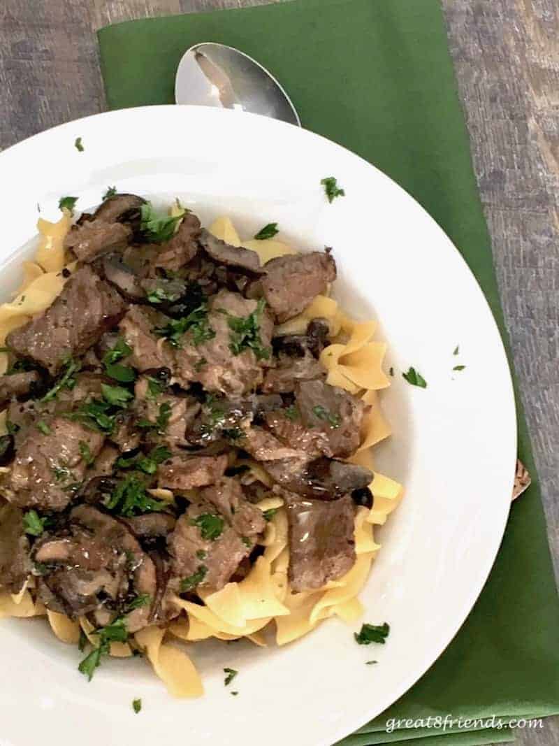 Overhead shot of beef stroganoff over noodles in a white bowl.