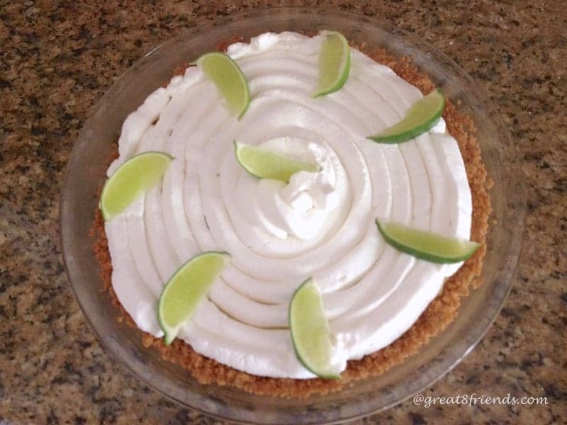 Overhead shot of key lime pie covered with whipped cream and garnished with lime wedges.