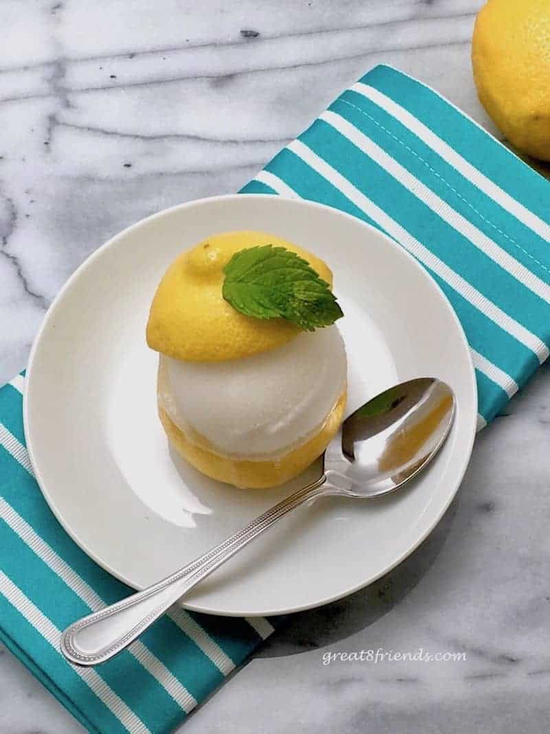 Overhead shot of Lemon Sorbet in a Lemon Cup on a white plate sitting on a blue and white striped napkin.