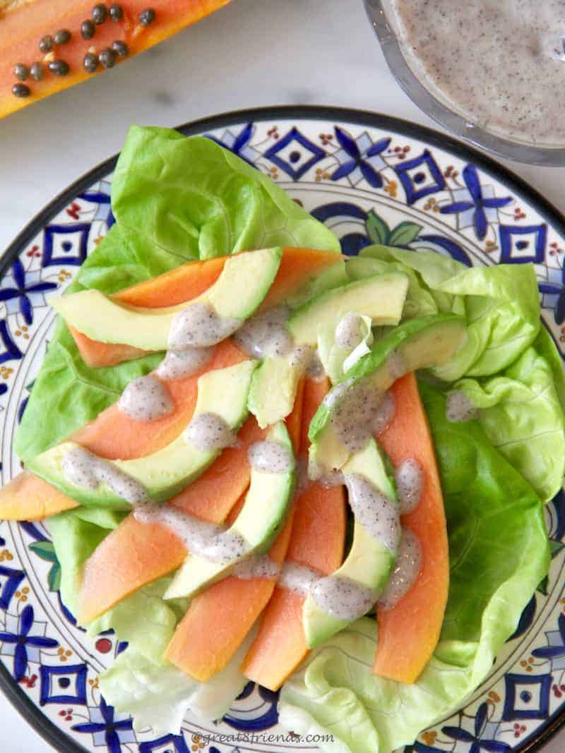 Papaya and Avocado Salad served on a blue and white plate with butter lettuce and poppyseed dressing drizzled on top.