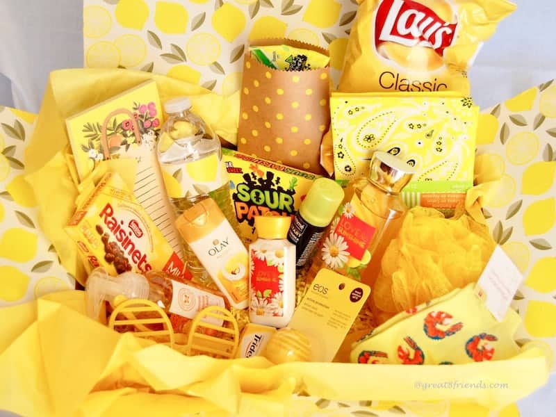 A yellow box filled with yellow tissue paper and yellow items, Lays potato chips, raisinets, olay cream, yellow sour patch kids, yellow note pad, etc.