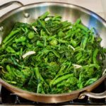 Cooked broccoli rabe in a copper and stainless steel pan with slivers of garlic.