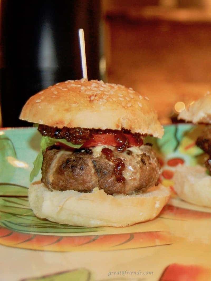 A Cambozola beef sliders with Bacon Jam, arugula and a sliced tomato on a sesame seed bun.