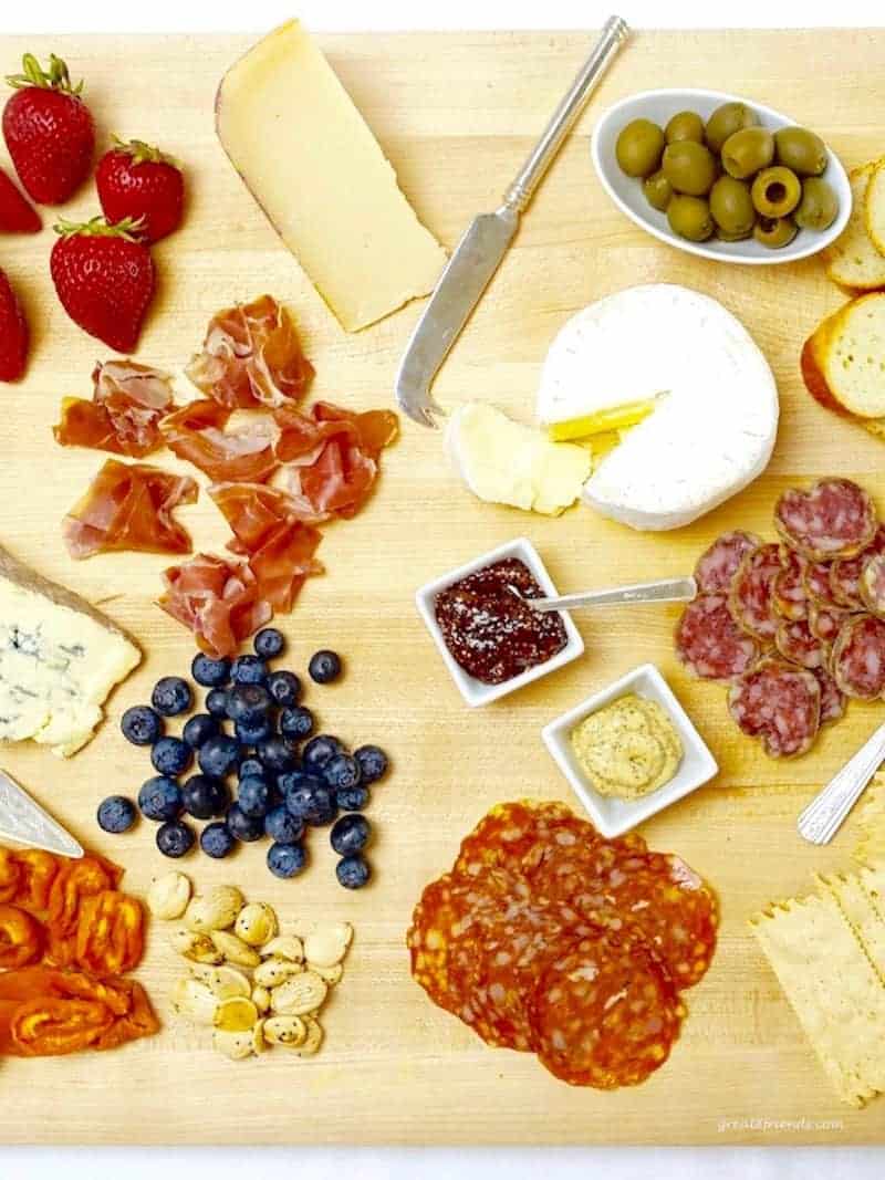 A Cheese and Charcuterie Board including fruit, nuts, crackers, olives and bread slices.