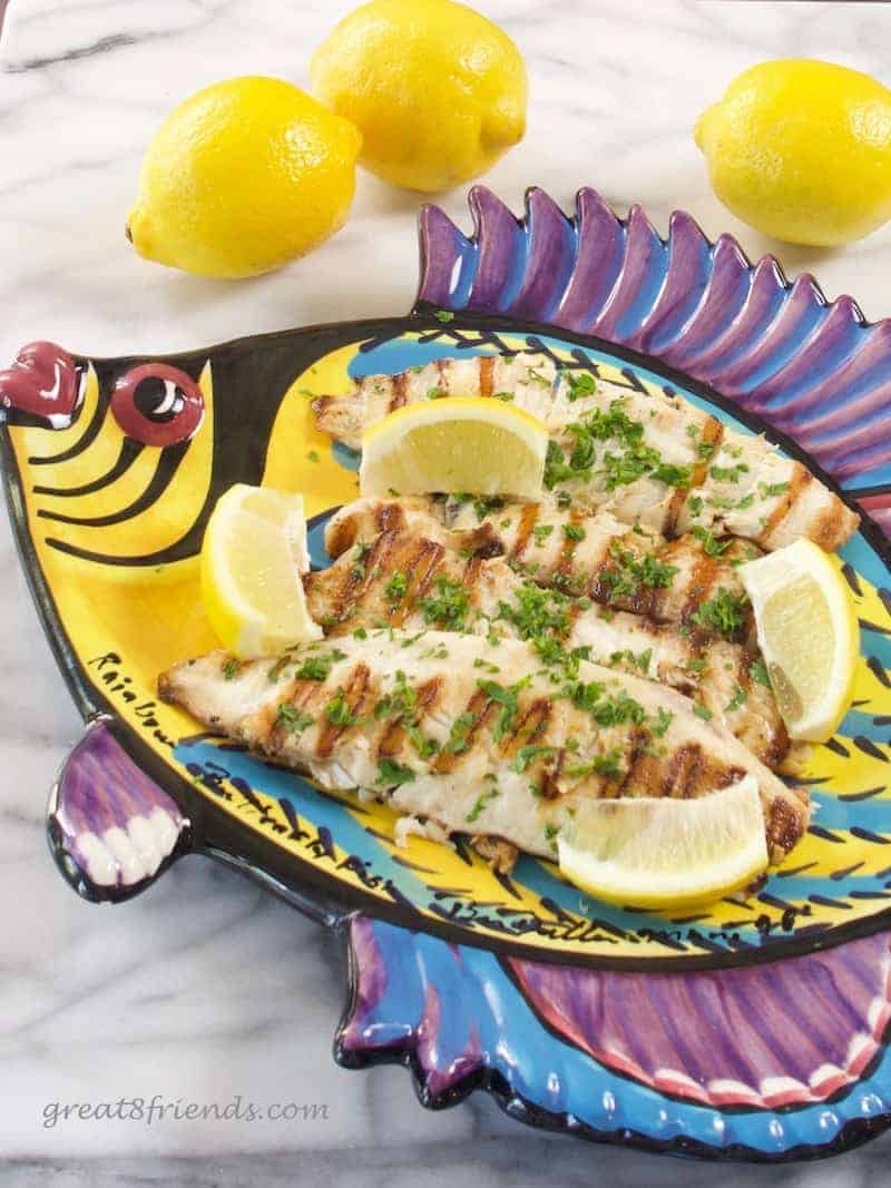 Grilled fish on a colorful fish shaped platter with lemons and parsley for garnish for fish Friday recipes.