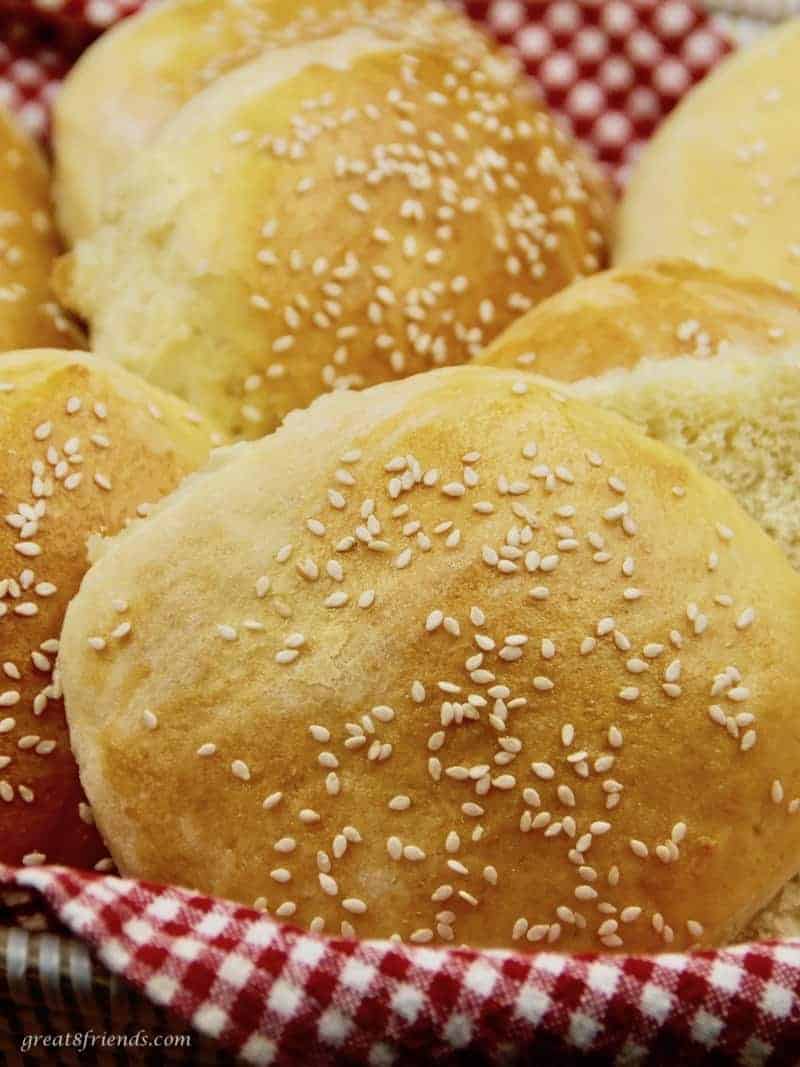 Several homemade sesame seed hamburger buns in a basket.