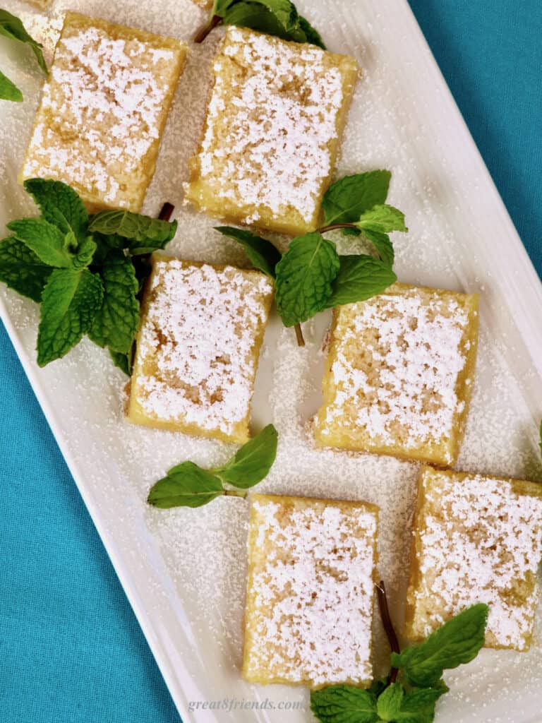 Lemon bars on white tray garnished with mint leaves.