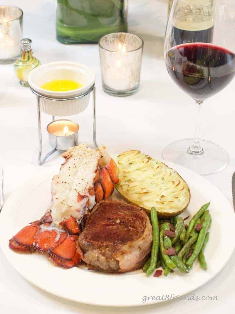 Meal of Lobster Tails with Clarified Butter, potato, filet, and green beans. With a glass of red wine and candlelight.