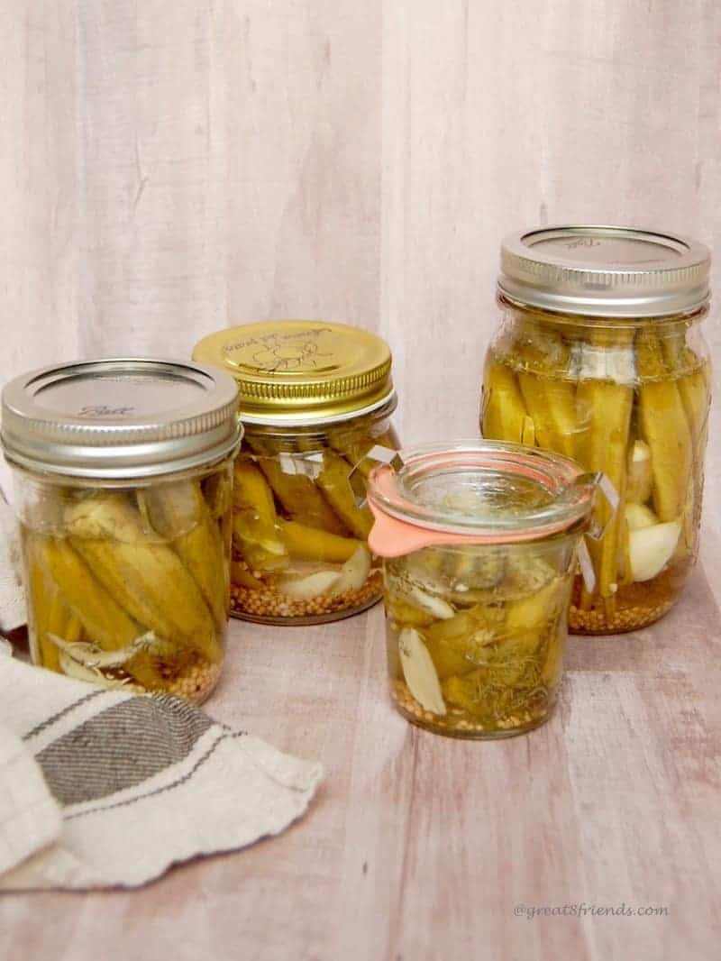 Four jars of pickled okra on a wood table.