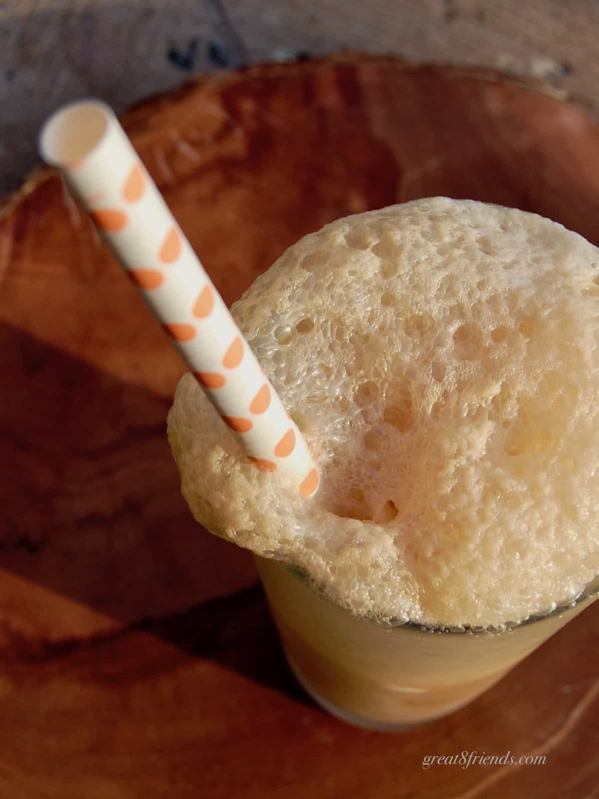 An overhead shot of the top of one frothy soda with an orange polka dotted straw.