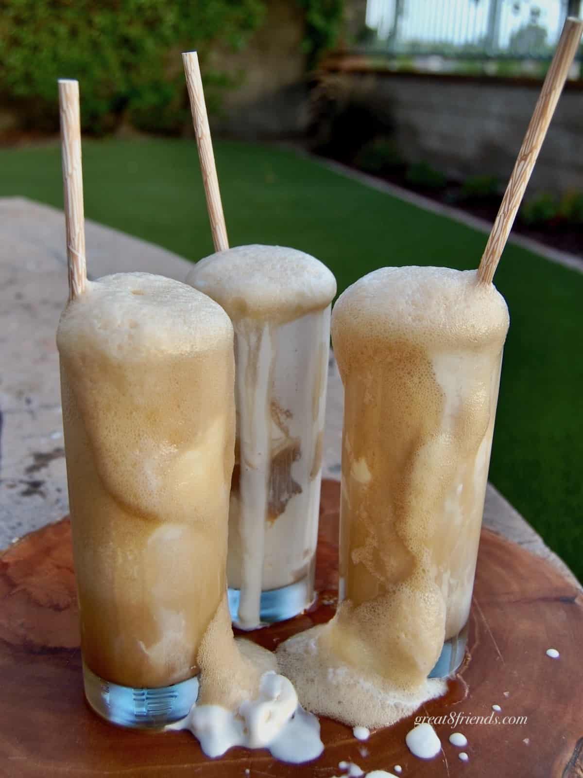 Three frothy root beer floats in tall glasses with straws.