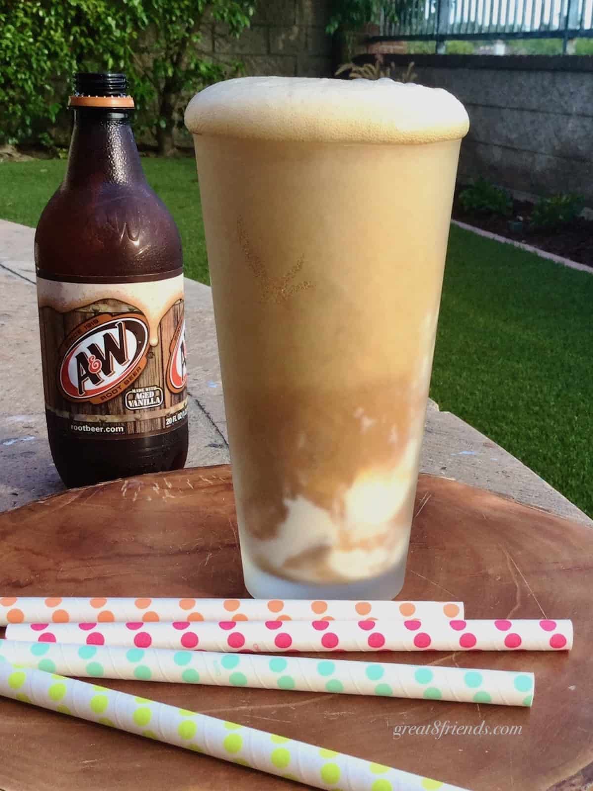 One tall root beer float with a bottle of A&W in the background and several colorful straws laying in front.