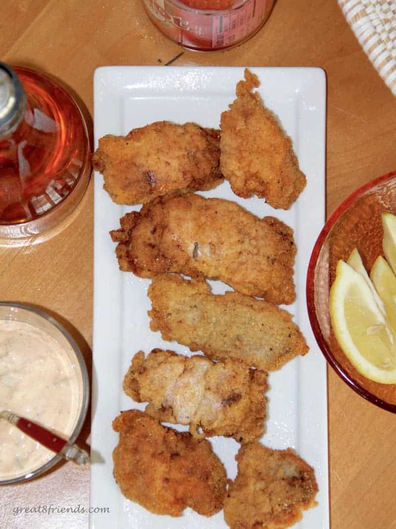 Overhead shot of fried catfish with a sauce and lemon wedges on the side.