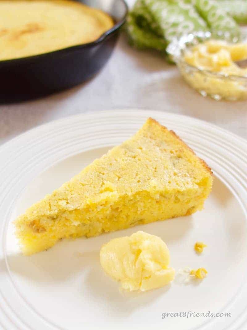 A wedge of cornbread on a white plate with a dollop of butter.