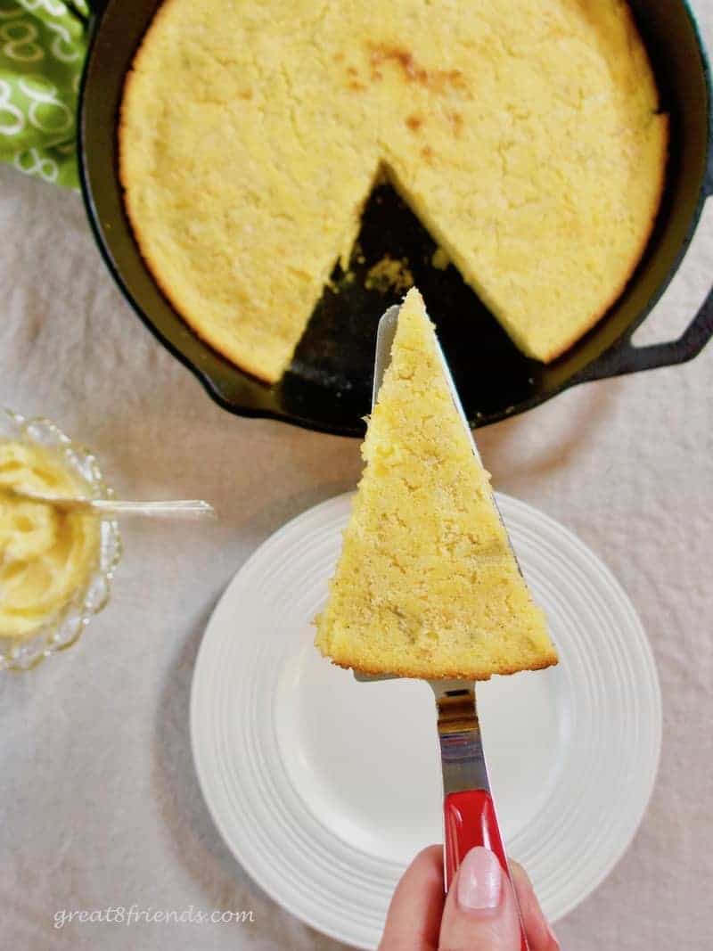 An overhead shot of skillet cornbread in the skillet with a slice cut and lifted up to the camera.