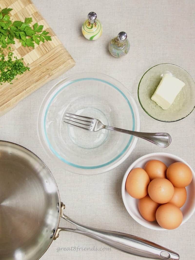 The ingredients for an omelette. A bowl, a fork, salt and pepper, butter, eggs, parsley and a pan.