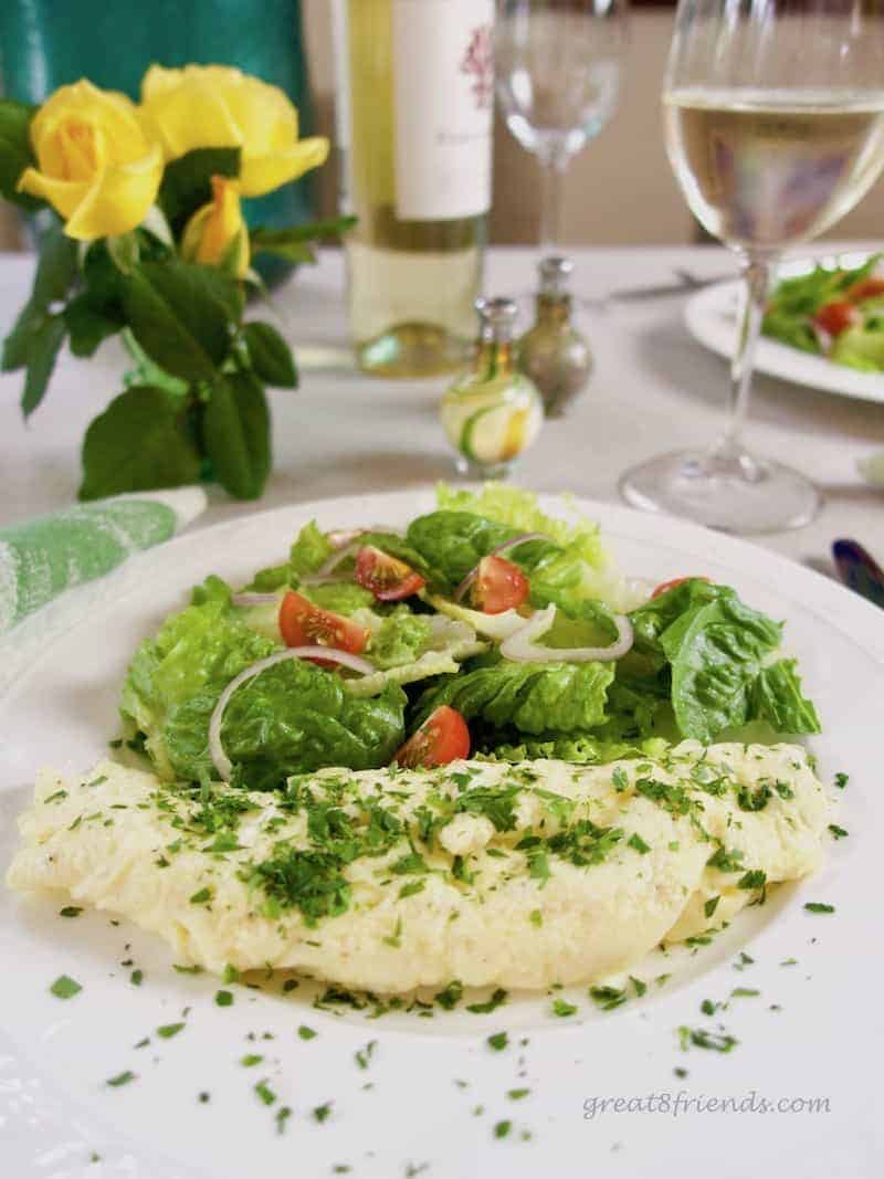 An omelette roulée with a small salad a glass of white wine and some yellow roses.