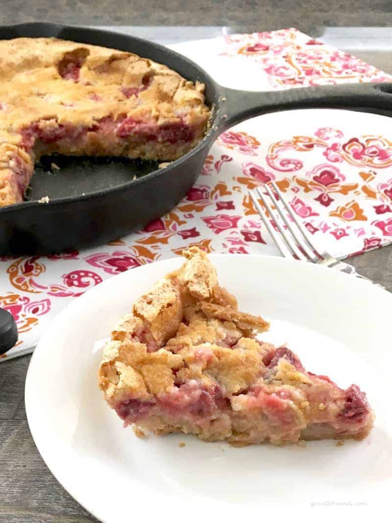 A slice of rhubarb tart on a white plate with the rest of the tart in a skillet in the background.