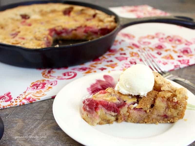 A slice of tart topped with a scoop of vanilla ice cream with the cast iron skillet in the background.