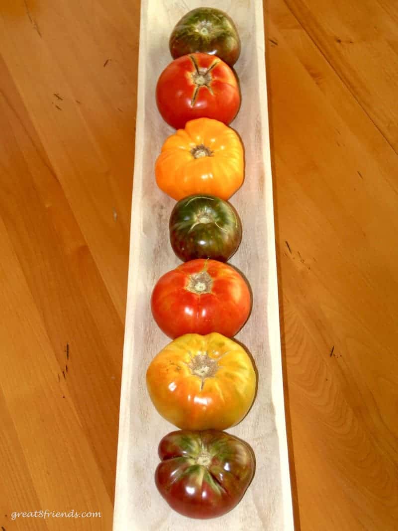 Heirloom tomatoes lined up vertically in a wood long bowl on a wood table.