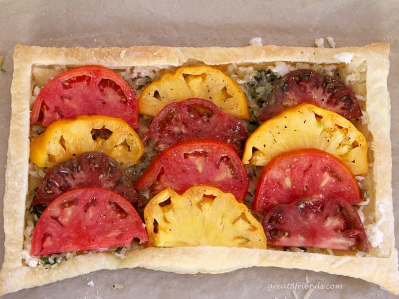 heirloom tomatoes on top of cooked onions on a baked puff pastry sheet. 