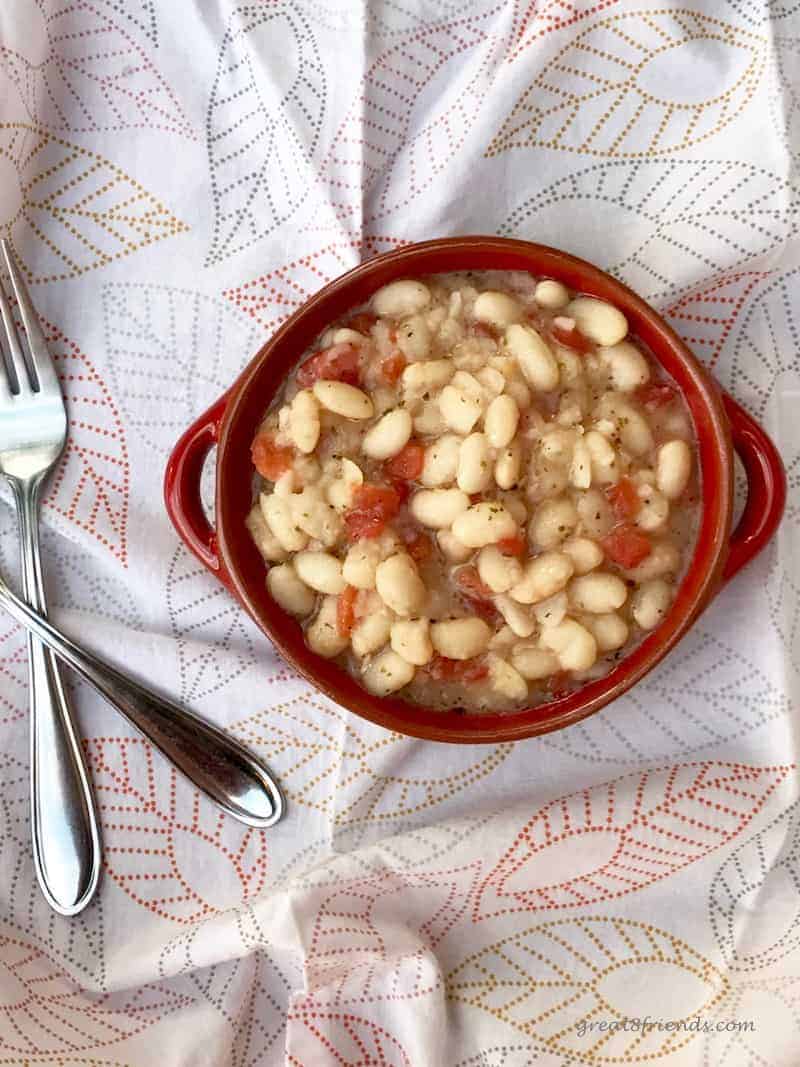 Overhead shot of the white beans and tomatoes in a round red bowl with a fork on one side.