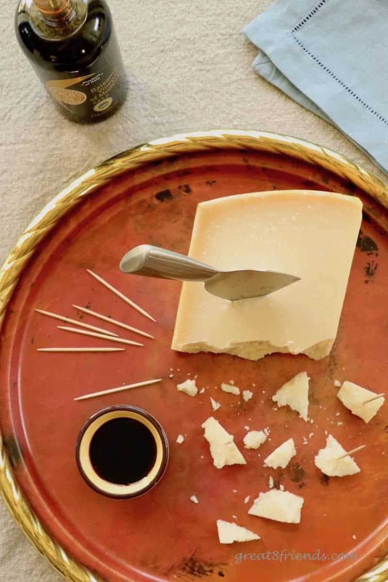 Balsamic Vinegar in the foreground with Parmigiano Reggiano with small pieces broken off and a small bowl of balsamic vinegar in the background.