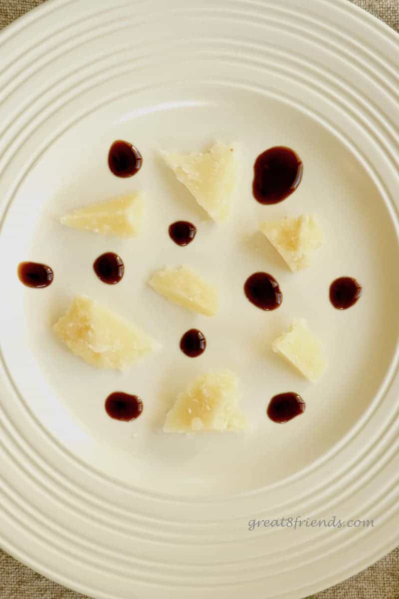 Overhead shot of white plate with hunks of Parmigiano Reggiano and dots of balsamic vinegar.