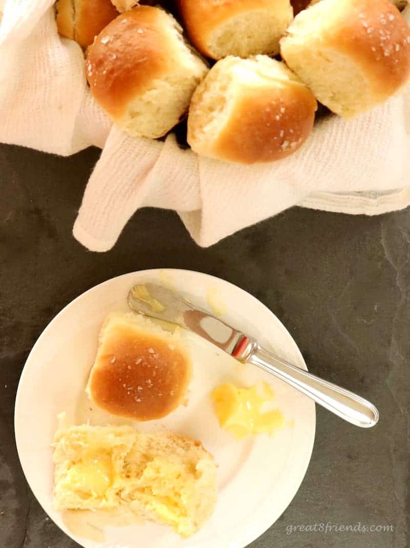 A dinner roll cut in half on a plate with some butter and the basket of rolls.