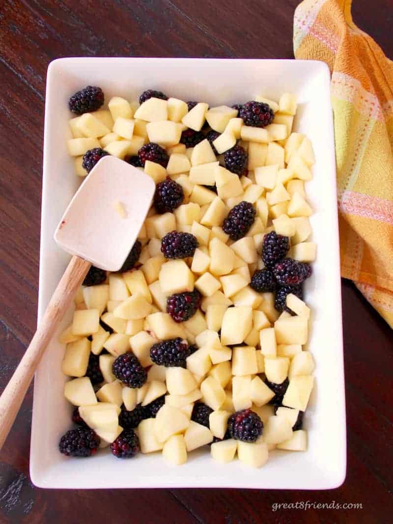 Raw cubed apple pieces and blackberries in a baking dish.