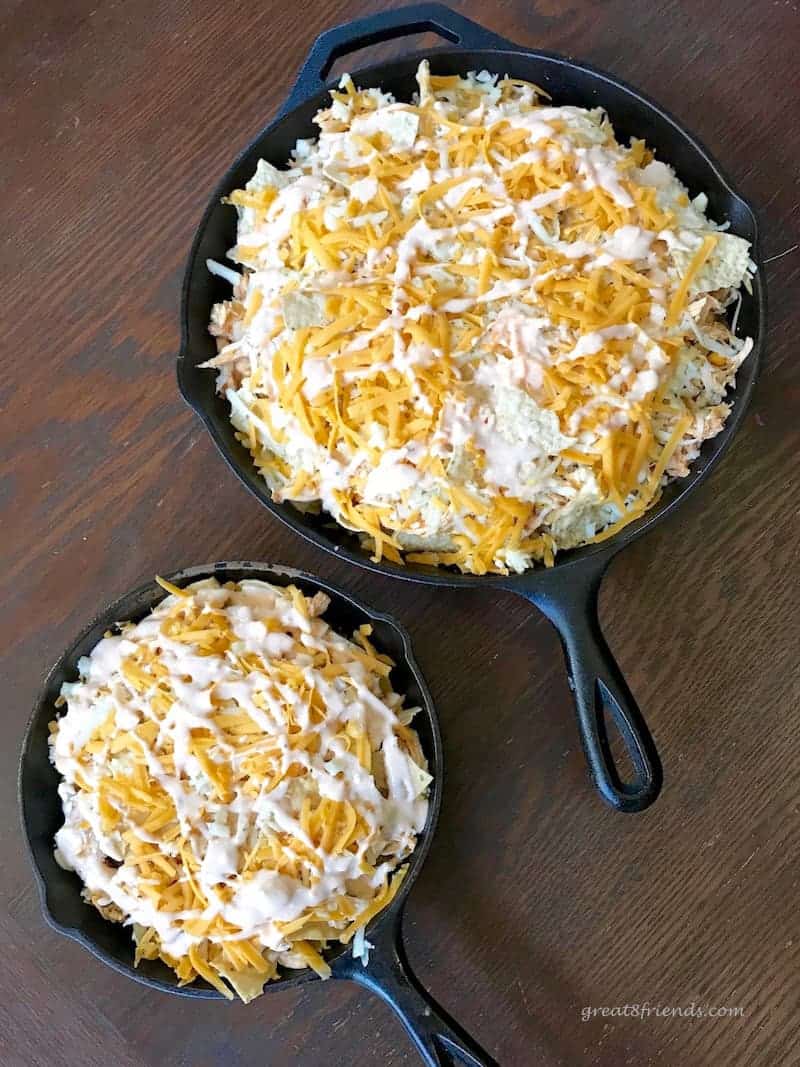 Overhead shot of two cast iron skillets full of cheesy buffalo chicken nachos ready to go in the oven.