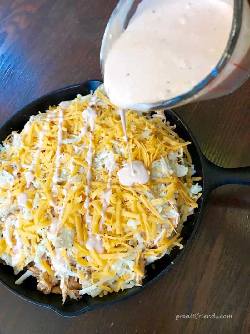 Buffalo sauce being poured over nachos.