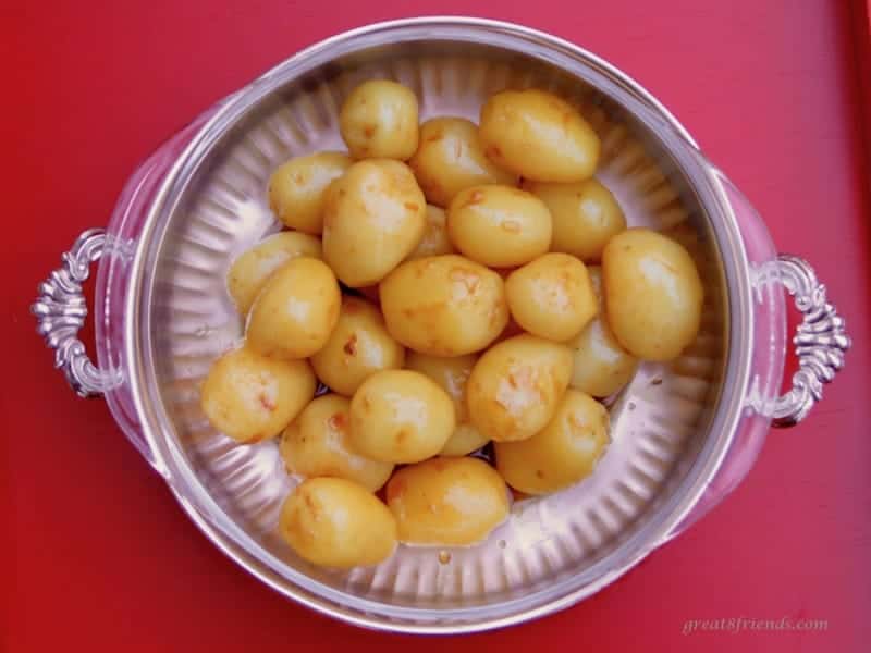 Caramelized Potatoes in a silver bowl on a red background.