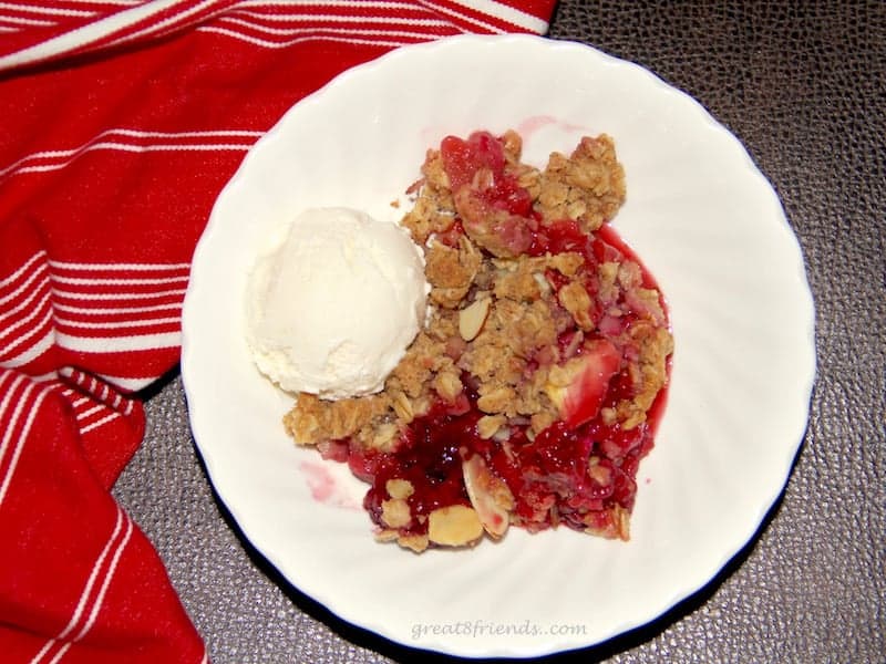 One serving of apple and blackberry crisp with one scoop of ice cream in a white bowl with a red napkin on the side. 