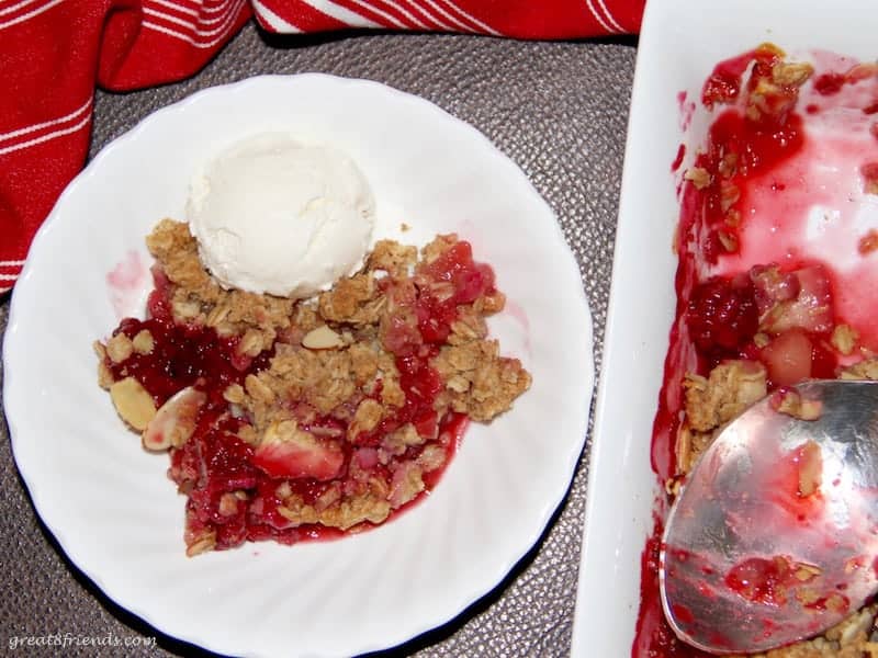 One serving of a berry crisp with apples served with one scoop of ice cream and the serving pan with spoon next to it.