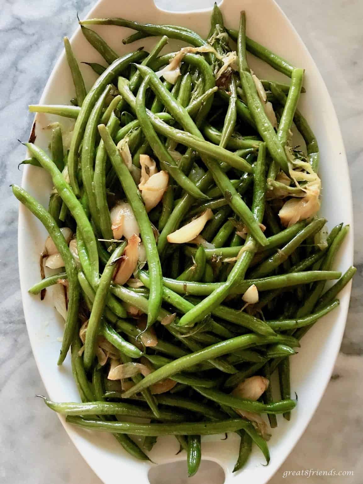 Overhead shot of green beans and onions on a white platter.