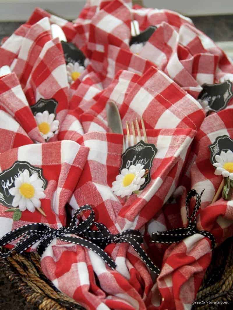 Red and white napkins wrapped around utensils with a daisy.