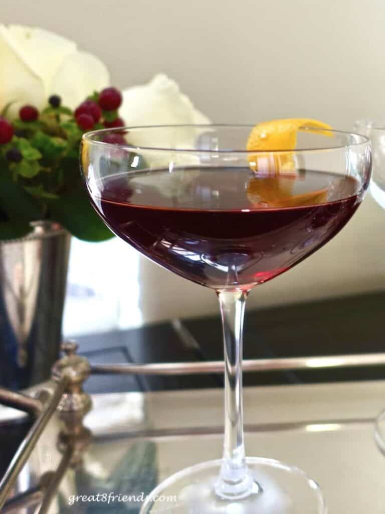 A Cherry Manhattan Cocktail in a coupe glass on a silver tray with an orange zest garnish.