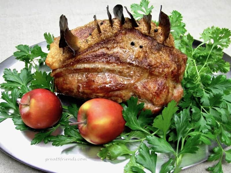 Roast Pork laying on a bed of parsley surrounded by apples.