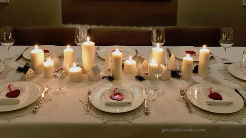 Table set for Christmas with candles down the center, white plates with red glass hearts.