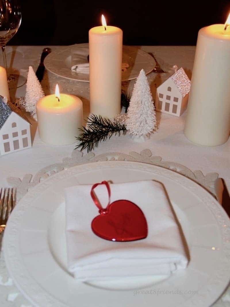 A Danish Christmas Dinner place setting with lit candles and small paper house and fir trees