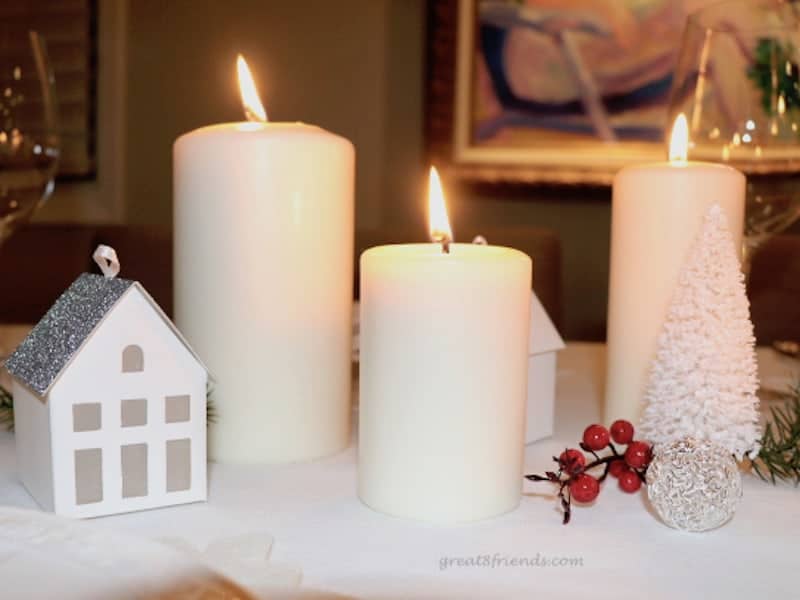 A close of Christmas centerpiece with lit candles and small paper house.