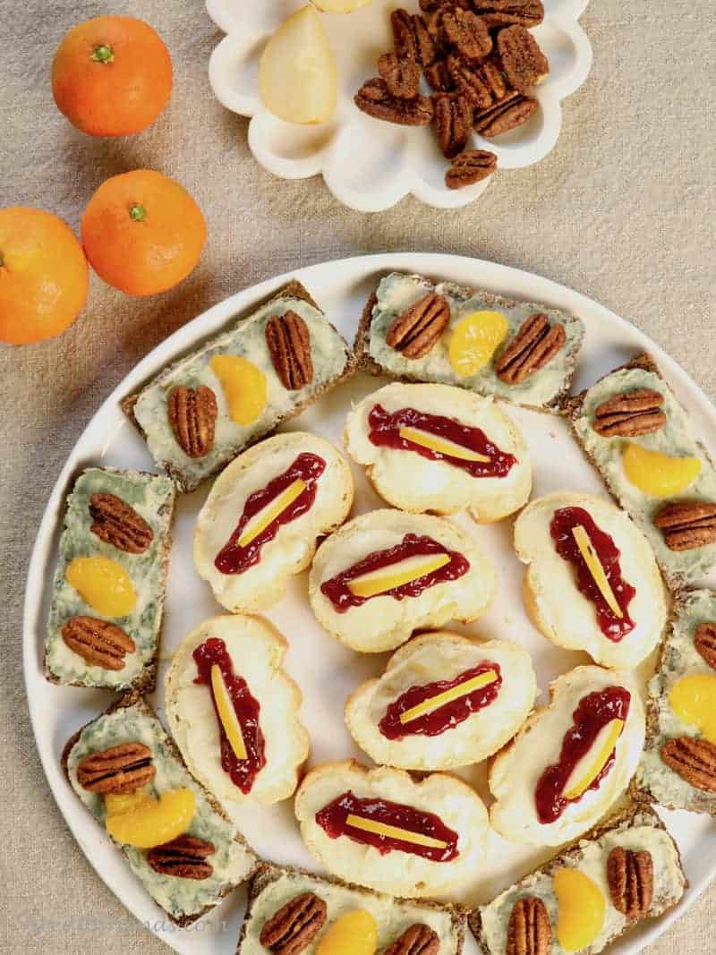 A round tray of cheese and fruit open faced sandwiches.