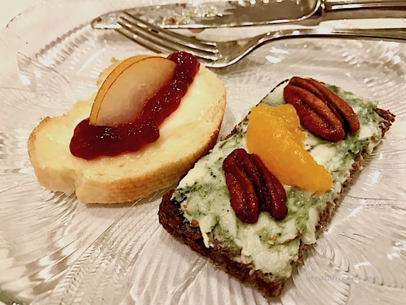 A plate with two pieces of cheese and fruit smorrebrod.