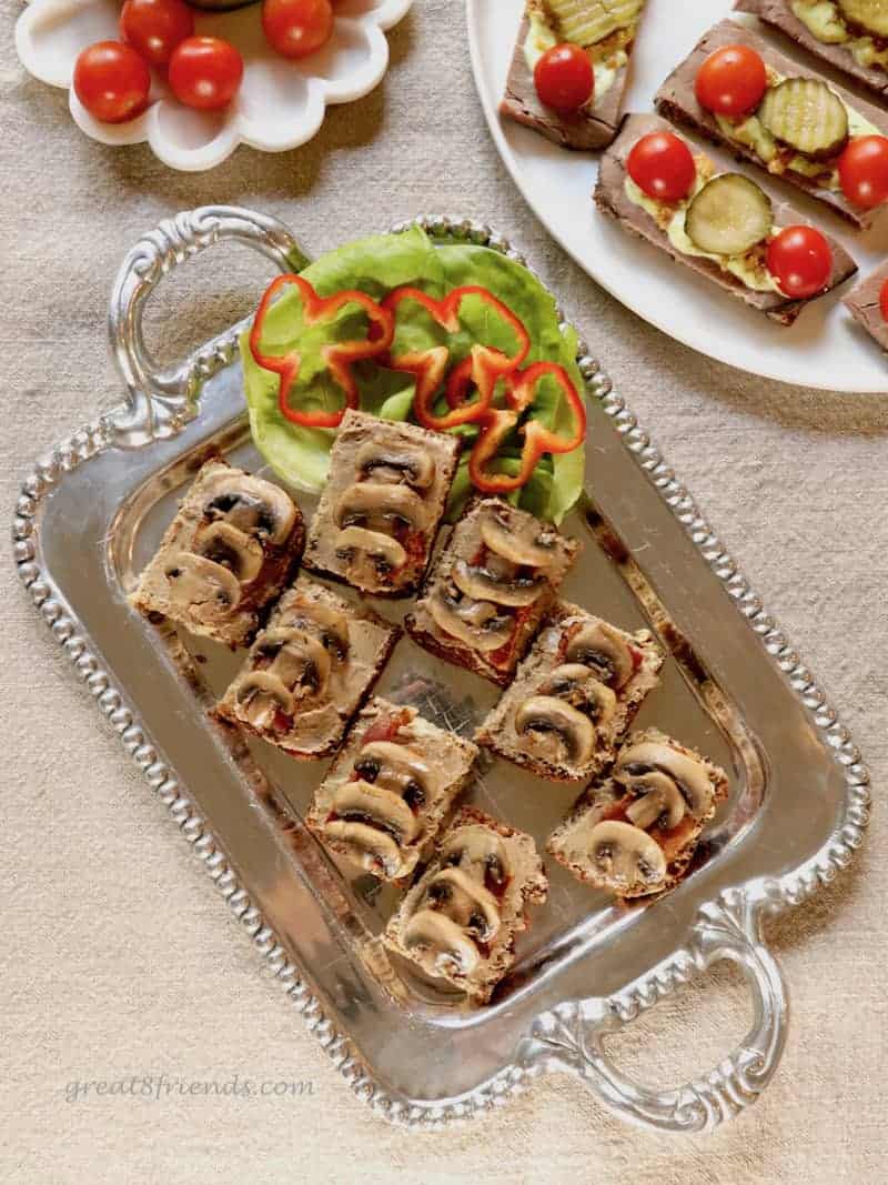 An aluminum tray of pate and mushroom open faced sandwiches.