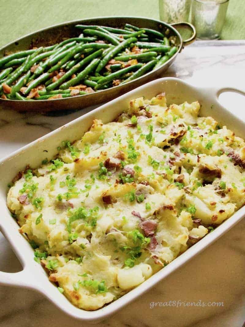 Cheesy Smashed Potato Casserole with green beans behind.