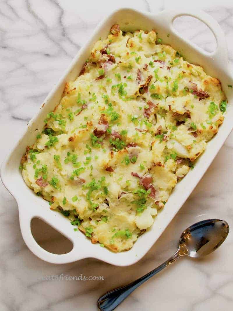 Overhead shot of cheesy smashed potato bake in a white ceramic casserole