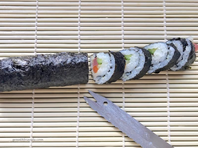 A sushi roll wrapped in seaweed being cut.