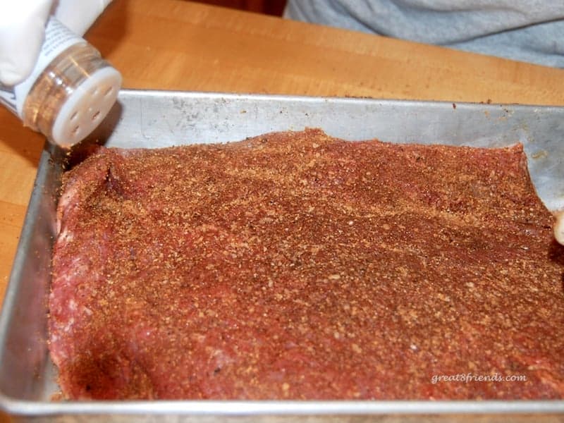 Uncooked brisket being sprinkled with dry rub.